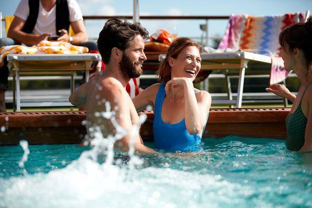 Geselliges Bordleben im Pool – Paar lächelt sich an und plaudert mit Mitreisenden