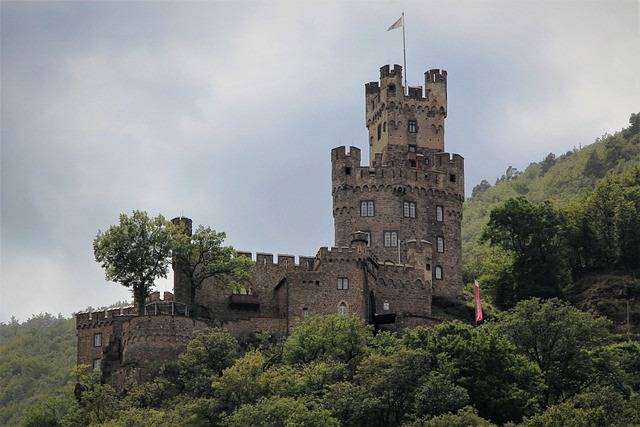 Burg auf bewaldetem Hügel umgeben von grüner Flusslandschaft