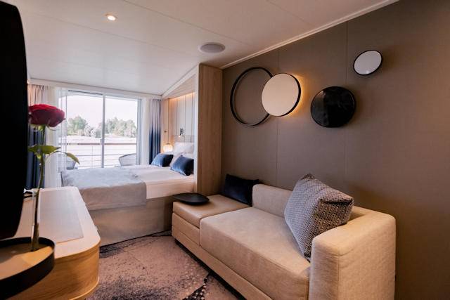 Große Balkonkabine auf der A-ROSA SENA mit gemütlichem Sofa, weitem Fenster und privatem Balkon mit Flussblick